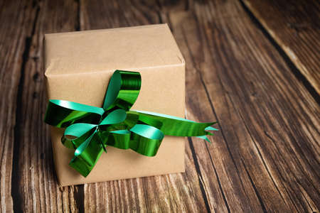 A closeup of a gift box with a green ribbon on wooden background