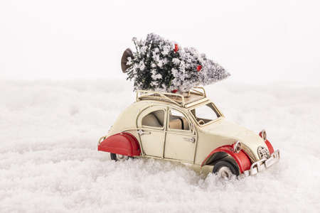 A closeup of a small vintage toy car with a Christmas tree on its roof on an artificial snowの写真素材