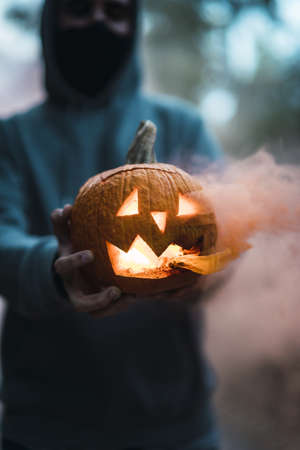 A vertical shot of a man holding a carved pumpkin with an orange smoke - the concept of Halloweenの写真素材