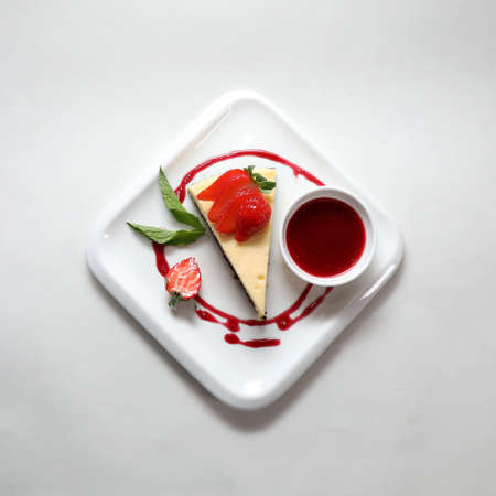 A top view of a piece of cheesecake with a strawberry on a plate isolated on a white background