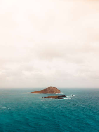 A small island in the ocean under the cloudy skyの写真素材