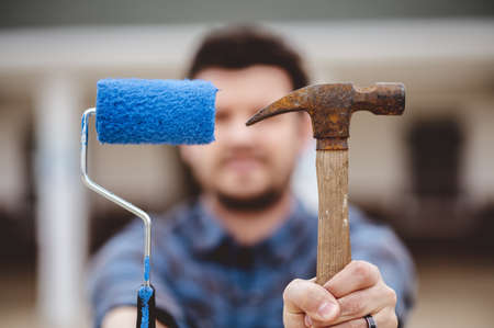 A soft focus of a man holding a paint roller with blue paint and an old rusty hammerの写真素材