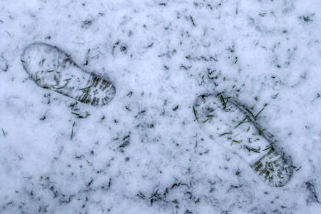 A top view shot of footsteps of male shoes in fresh white snow in winter