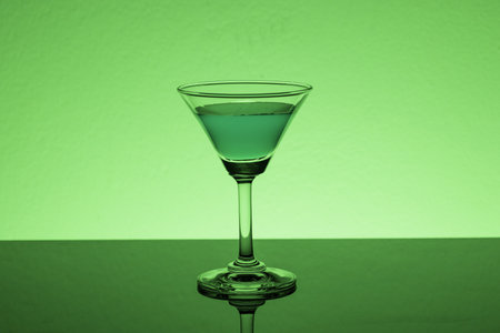 A closeup shot of an alcoholic drink reflecting on the glass of the table under a green light on a green backgroundの写真素材