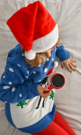 A vertical shot of a Caucasian blonde woman wearing Christmas clothes and drinking coffee from a ...