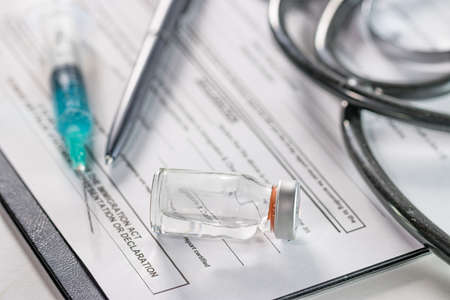 A closeup of an ampoule and a needle syringe on a document with a phonendoscope on the background