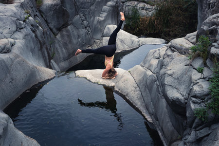 A beautiful shot of a fearless young woman doing yoga near a high rocky mountain riverの写真素材