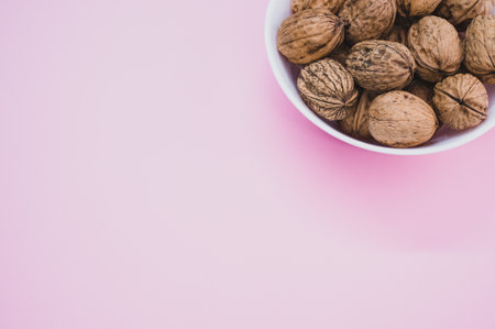 A top view of walnuts on a white bowl isolated on a pink background