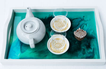 A high angle closeup shot of a teapot and Turkish teacups on a tray with epoxy resin artの写真素材