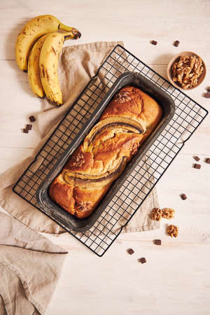A vertical shot of delicious banana bread in a loaf pan with chocolate chunks and walnut on a tableの写真素材