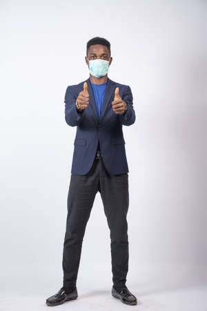 A young Black male wearing a suit and face mask standing confidently giving a thumbs-up - the new normal conceptの写真素材