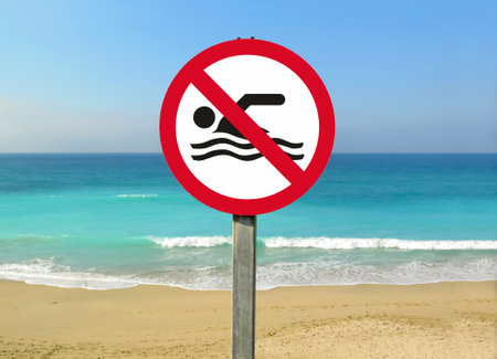 A view of a no swimming sign on the beach with calm sea captured on a sunny dayの写真素材