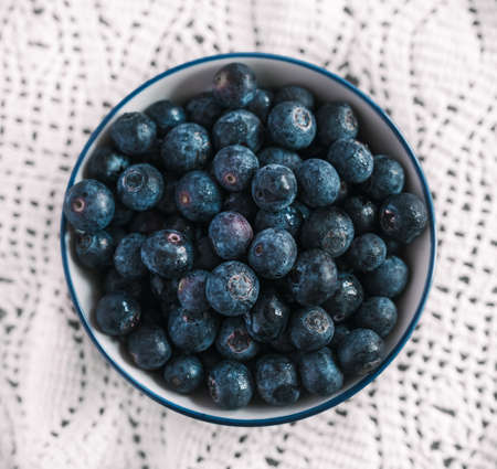 A high angle shot of a bowl filled with blueberries on a nice white tablecloth on a tableの写真素材