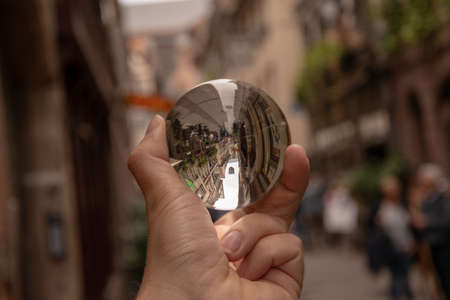 A closeup shot of a person holding a crystal ball with the reflection of historic buildings