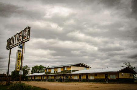 A rusty metal motel sign with wooden old motels under the cloudy and rainy  skyの写真素材