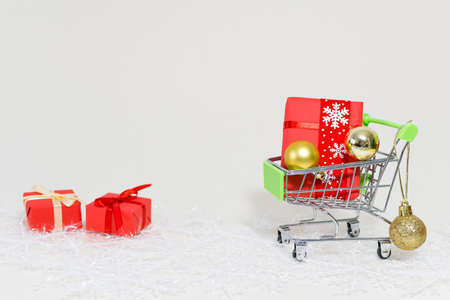 A shopping trolley with gift boxes and golden spheres on a snowflake on a white backgroundの写真素材