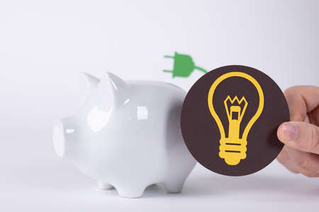 A light bulb sign near a piggy bank- a concept of electricity price