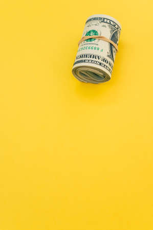 A vertical shot of rolled-up dollar bills on a yellow surfaceの写真素材