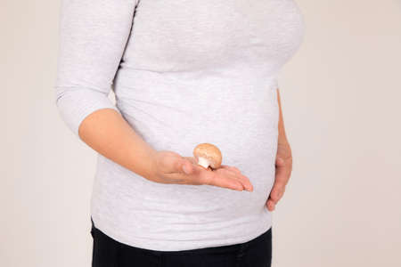 A closeup shot of a pregnant woman holding a mushroom showing the size of her baby
