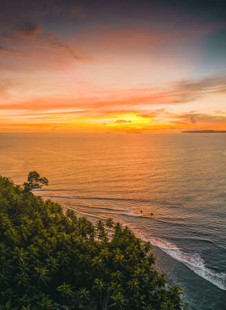 The mesmerizing view of the calm ocean and the trees in the shore during sunset in Indonesiaの写真素材