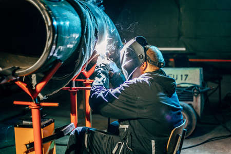 A shallow focus of a welder wearing a protective helmet and welding steel in a factoryの写真素材