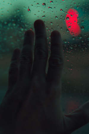 A man's hand against a glass with rain dropsの写真素材