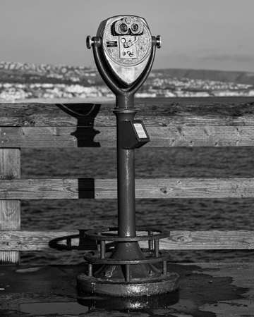 A vertical grayscale shot of sightseeing binoculars on a pierの写真素材
