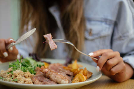 A selective focus shot of a female eating a dish with steak and potatoの写真素材
