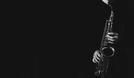 A grayscale shot of a cool and handsome guy playing his saxophone isolated on a dark backgroundの写真素材