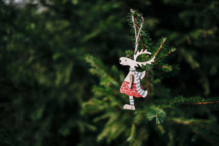 A closeup of a cute wooden deer-shaped Christmas ornament hanging from a pine treeの写真素材