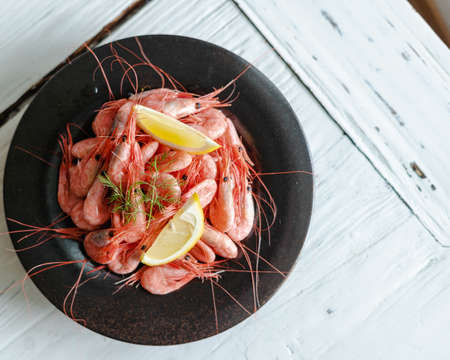 A high angle shot of a plate of Botan shrimps with lemon on a white wooden surfaceの写真素材
