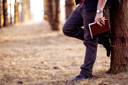 A selective focus shot of a man holding a book posing in a forestの写真素材