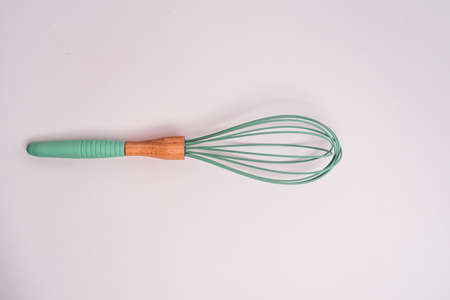 A closeup shot of a green kitchen whisk isolated on a light-colored backgroundの写真素材