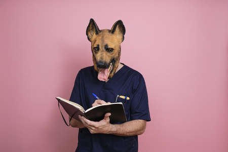 A young man in a latex dog head mask taking some notes on a pink backgroundの写真素材