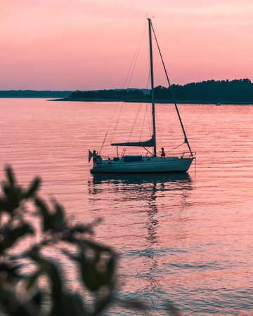 A vertical shot of a sailing boat in the sea during sunsetの写真素材