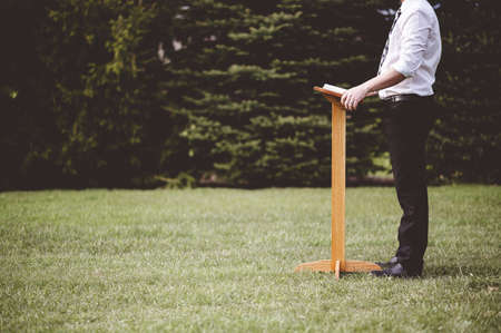 A man standing near a wooden stand with a book on it in the parkの写真素材