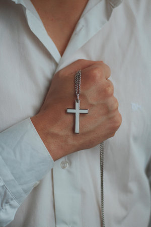A closeup shot of a religious male holding a silver necklace with a cross pendantの写真素材