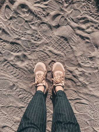 A top view shot of female legs in cream sneakers on the sand, walk on a sandy beach