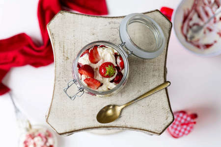 A horizontal shot of a jar of strawberries and white cream served on a square plate with a spoonの写真素材