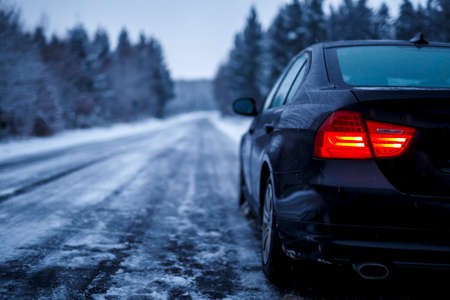 A black car on an iced road surrounded by trees covered with snowの写真素材
