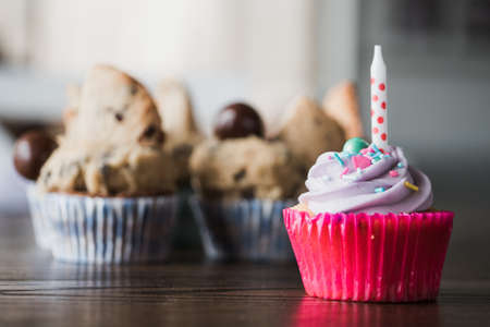 A beautiful closeup of a yummy pink cupcake against chocolate cupcakes on a wooden table - perfect background for pastry shopの写真素材