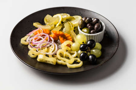 A plate with marinated pickles, pepper, onions and carrots with white and black grapes and olivesの写真素材
