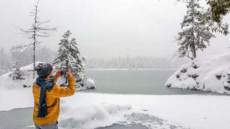 A view of a young male taking a photo of a frozen lake