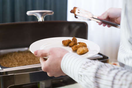 The man putting chicken nuggets on his plate in a cafeteriaの写真素材