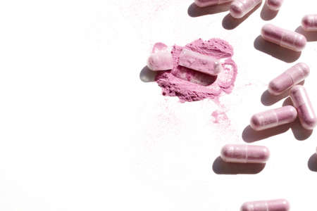 A high angle shot of some pink capsules with the internal powder scattered on a white surfaceの写真素材