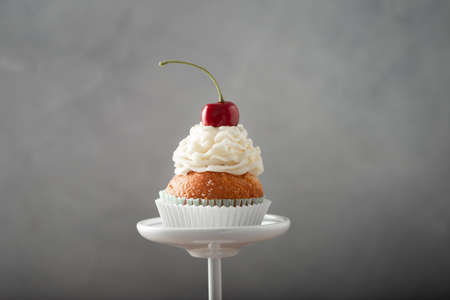 A closeup shot of a delicious cupcake with cream and cherry on top on a dessert standの写真素材