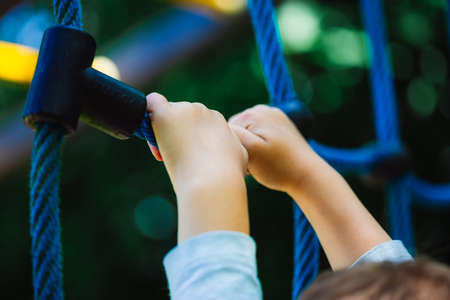 A low angle shot of a child holding on to a blue climbing toy on the playground of a parkの写真素材