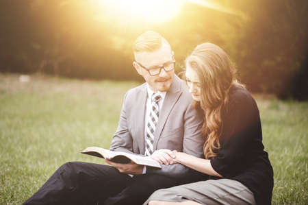 A beautiful couple sitting at the park and reading the Bible with bright sun rays in the backgroundの写真素材