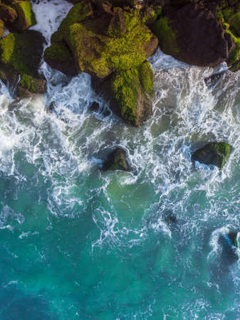 A vertical overhead aerial shot of a wavy blue sea against the rocksの写真素材