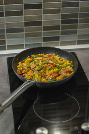 A vertical shot of a chicken dish with fried vegetables in a frying pan on the stove in the kitchenの写真素材